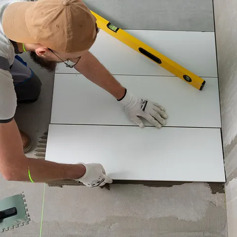 Flislegger legger store hvite fliser på gulv